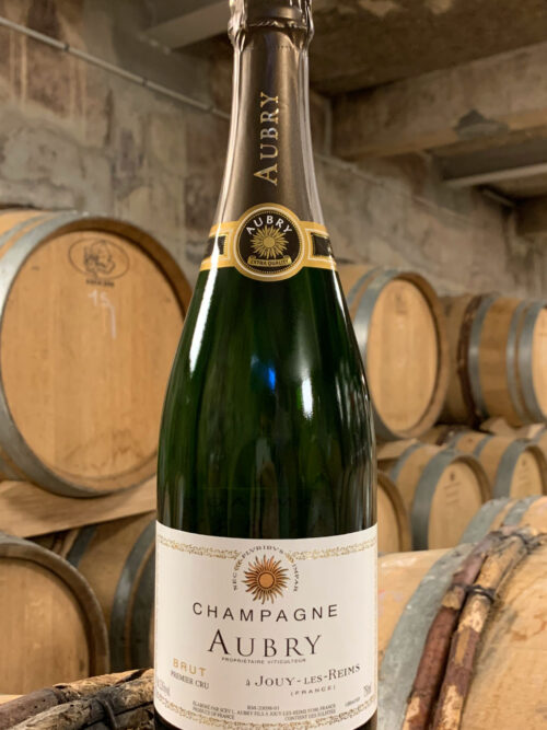 Photo d'une bouteille de Champagne Aubry Brut prise dans la cave aux côtés des fûts en chêne à Jouy-Les-Reims