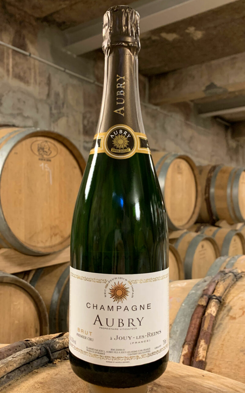 Photo d'une bouteille de Champagne Aubry Brut prise dans la cave aux côtés des fûts en chêne à Jouy-Les-Reims