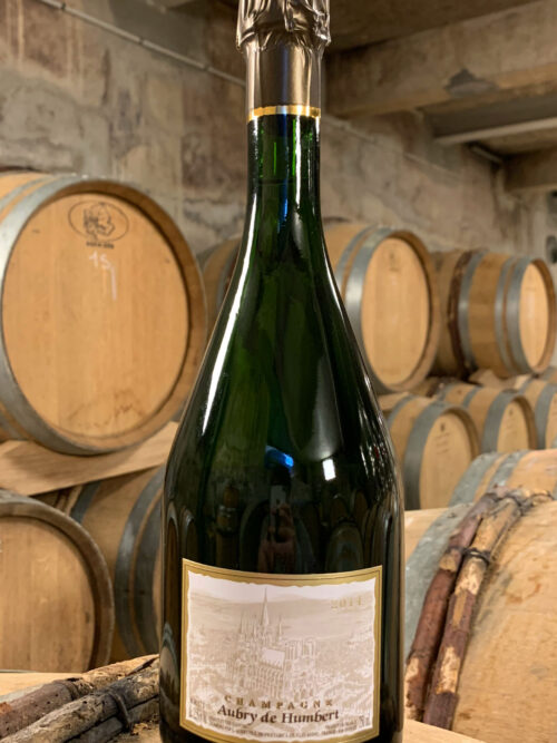 Photo d'une bouteille de Champagne Aubry de Humbert prise dans la cave aux côtés des fûts en chêne à Jouy-Les-Reims