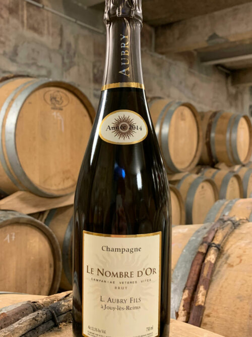 Photo d'une bouteille de Champagne Aubry Le Nombre d'Or Brut prise dans la cave aux côtés des fûts en chêne à Jouy-Les-Reims