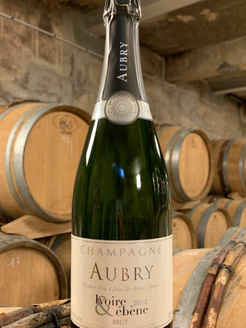 Photo d'une bouteille de Champagne Aubry Ivoire et Ébène prise dans la cave aux côtés des fûts en chêne à Jouy-Les-Reims