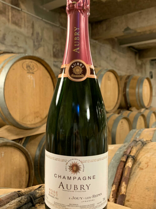 Photo d'une bouteille de Champagne Aubry Rosé prise dans la cave aux côtés des fûts en chêne à Jouy-Les-Reims