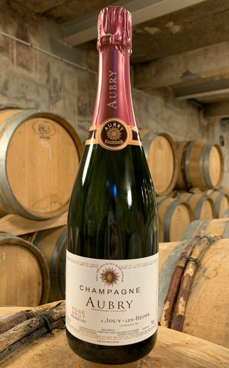 Photo d'une bouteille de Champagne Aubry Rosé prise dans la cave aux côtés des fûts en chêne à Jouy-Les-Reims