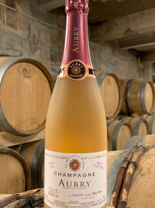 Photo d'une bouteille de Champagne Aubry Sablé Rosé prise dans la cave aux côtés des fûts en chêne à Jouy-Les-Reims